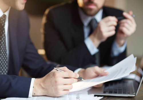 Successful Business Partners Discussing Contract Closeup portrait of two unrecognizable business partners reviewing paperwork and signing contract papers at table during meeting